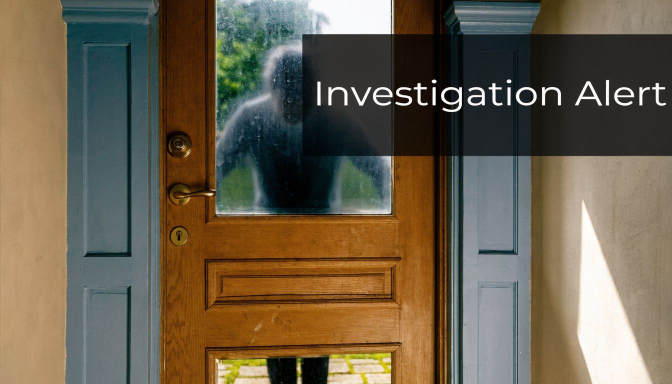 A blurry silhouette of a person standing outside looking through a wooden glass panelled front door.